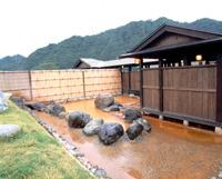 木造づくりの建物があり、周りには大きな石で囲まれた温泉の写真