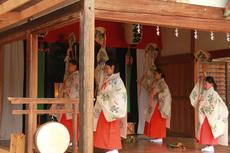 巫女装束を着用した4人が扇子を持ち右手を上に挙げている写真