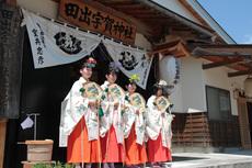 花の髪飾りを付け巫女装束を着用した女性4人が並んで扇子を持っている写真
