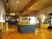 博物館の中央に黒いカーテンの台にガラスのケースに道具や生活用具が展示されている写真