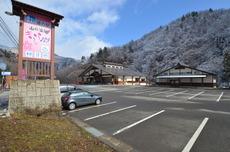 駐車場の左側に「道の駅山口温泉きらら289」と書かれた看板があり、広い駐車場の奥に茶色い屋根に白い壁の平屋建ての建物が2棟写っている写真