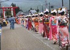 神社の赤い鳥居の方へ角隠しに艶やかな着物を着た女性たちが一列に並んで練り歩いている写真