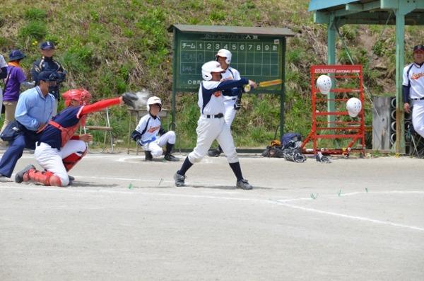 少年野球の試合でバッターの選手がバットを空振りし、キャッチャーがミットでボールを受けているのを審判や他の選手たちが見ている写真